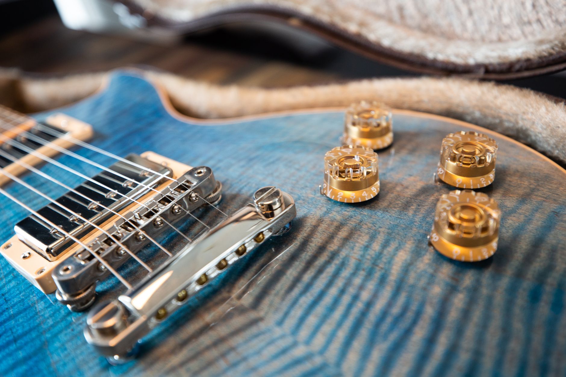 Detailed close-up of a blue electric guitar featuring gold control knobs and metal strings.
