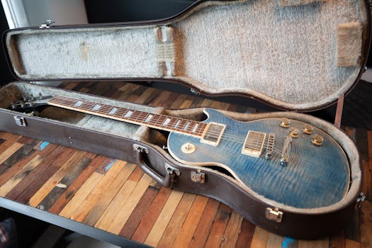 Close-up of a blue electric guitar in an open case on a wooden table, indoors.