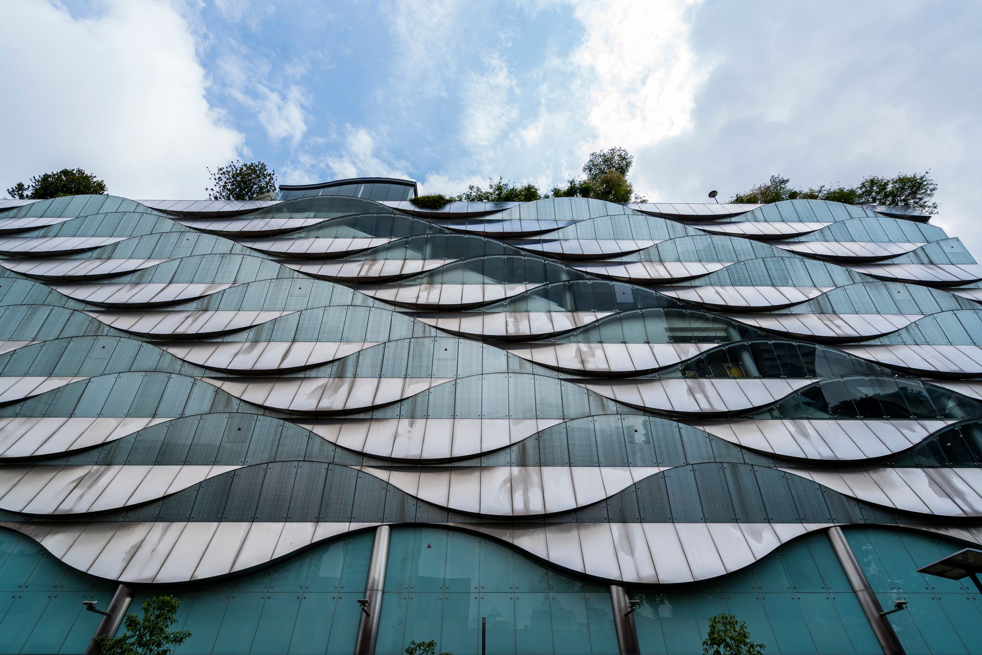 Futuristic building facade with wave-like glass patterns and greenery on top.