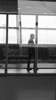 Black and white silhouette of lonely man standing in an airport corridor with seats and windows.