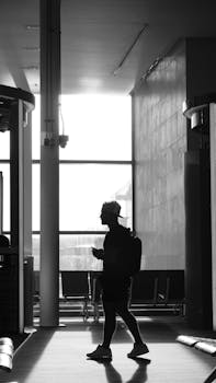 A silhouette of a man with a backpack walks through a sunlit airport terminal.