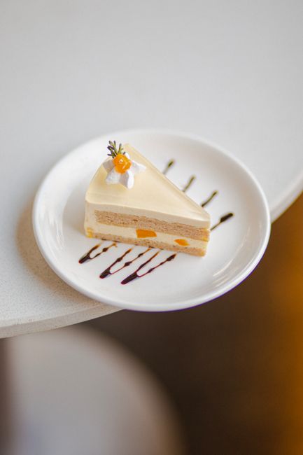 Delicious fruit-topped cream cake slice elegantly presented on a white plate, drizzled with sauce.