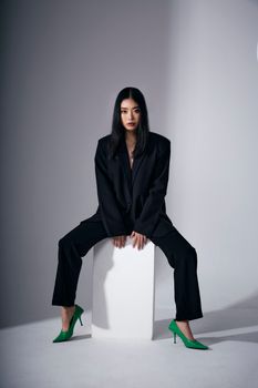 Striking fashion portrait featuring a woman in a black suit and green heels sitting on a block.