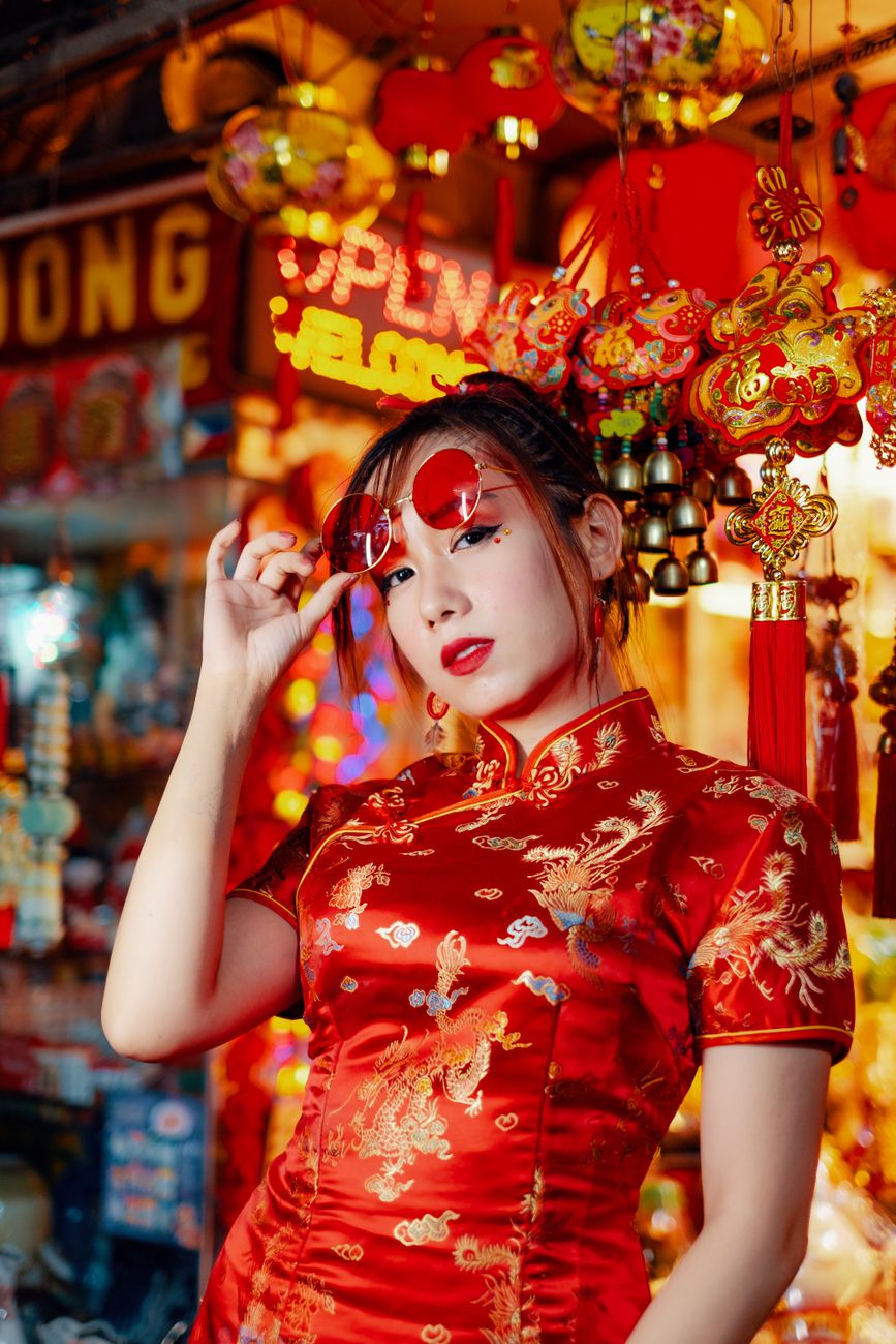 Asian woman in red traditional dress celebrating Chinese New Year in a vibrant market setting.