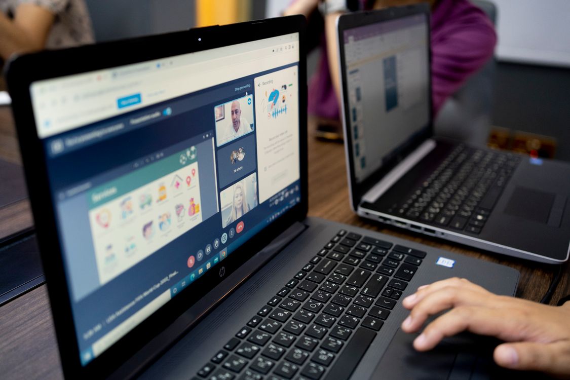 A person makes a video call on a laptop showing remote meeting participants in a split-screen view