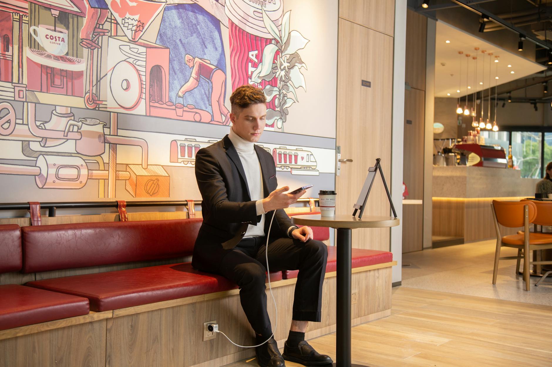 Businessman sitting in a stylish cafe, using smartphone while charging. Urban lifestyle concept.