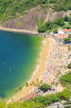 Vibrant aerial shot of Rio de Janeiro's bustling beach with colorful umbrellas and lush surroundings.