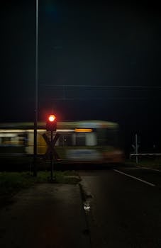 A train speeds past a level crossing at night in Bornheim, Germany, with a glowing red signal.
