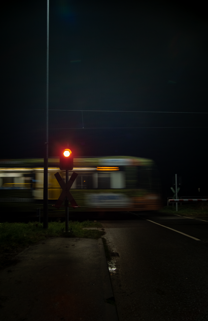 A train speeds past a level crossing at night in Bornheim, Germany, with a glowing red signal.