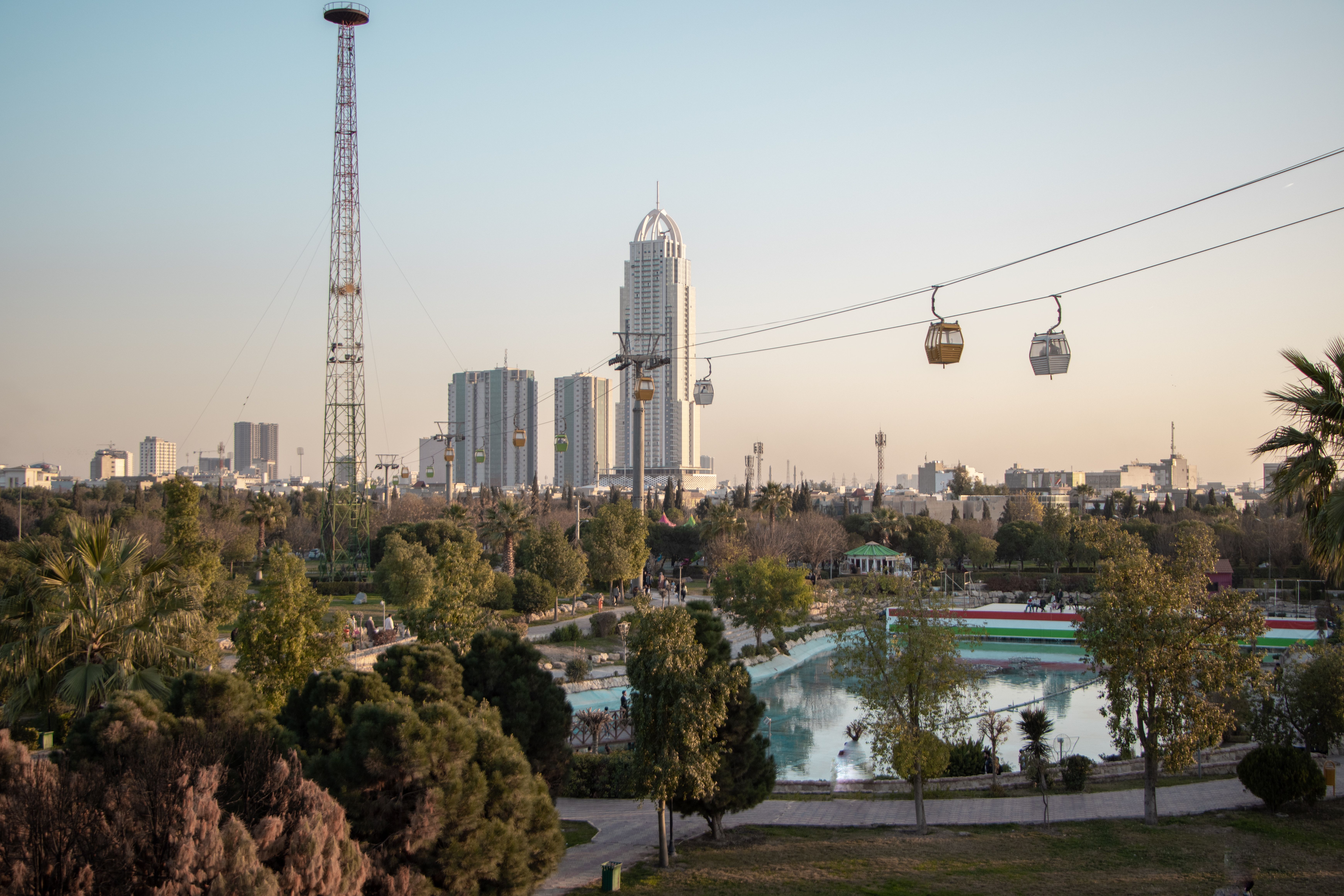 View of Erbil skyline featuring park, skyscrapers, and cable cars at sunset.