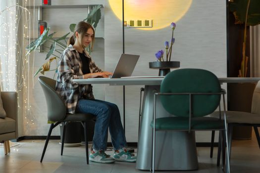 Young woman using a laptop in a stylish home office setting, showcasing a modern lifestyle.