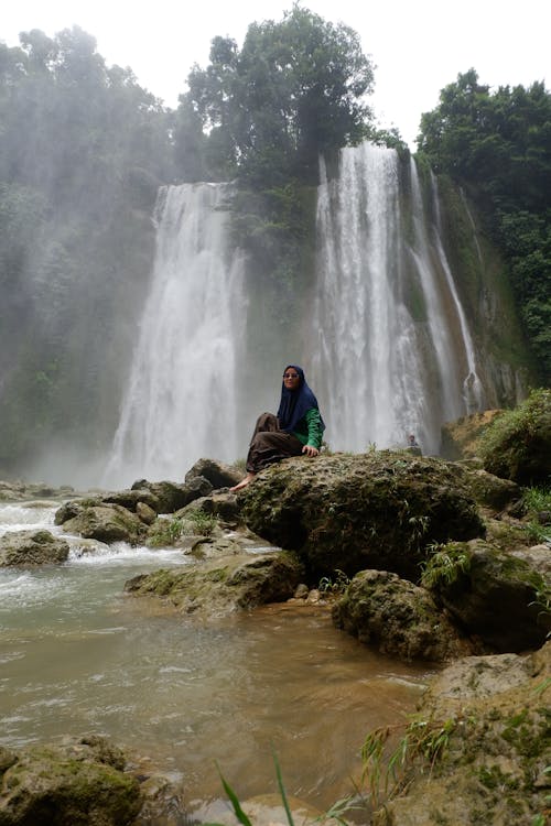 Woman Sitting on Rocks near Waterfall