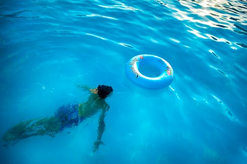 Person Swimming Under Body of Water Near Blue Inflatable Ring