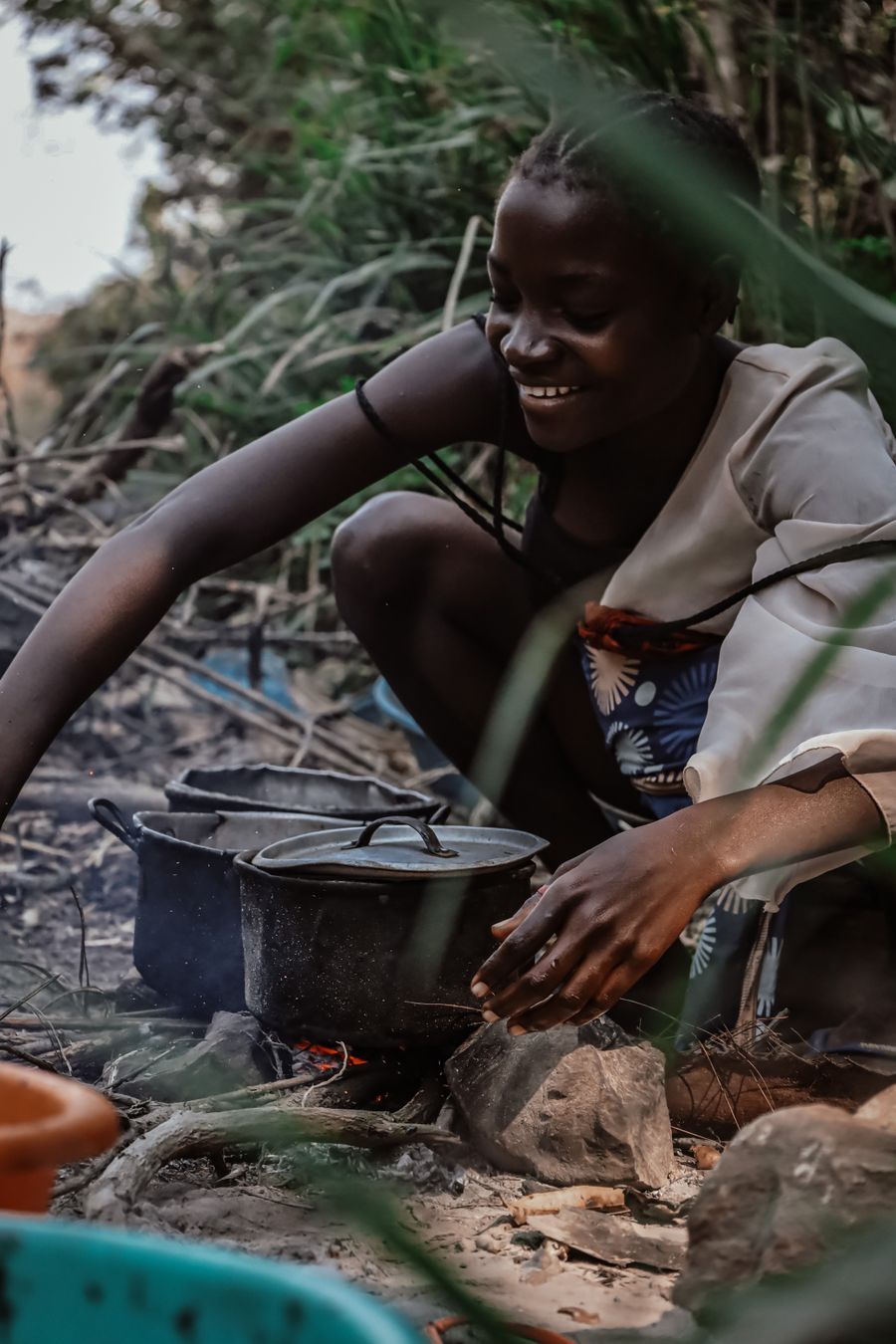 Smiling teenage girl cooking a communal meal over an open fire