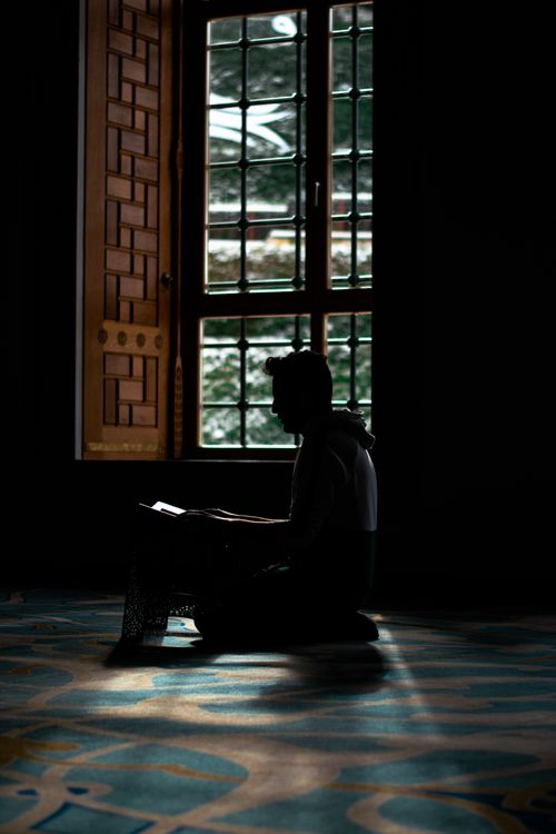 Free Silhouette of a man praying inside a mosque in Istanbul. Light filters through a wooden window, casting shadows. Stock Photo