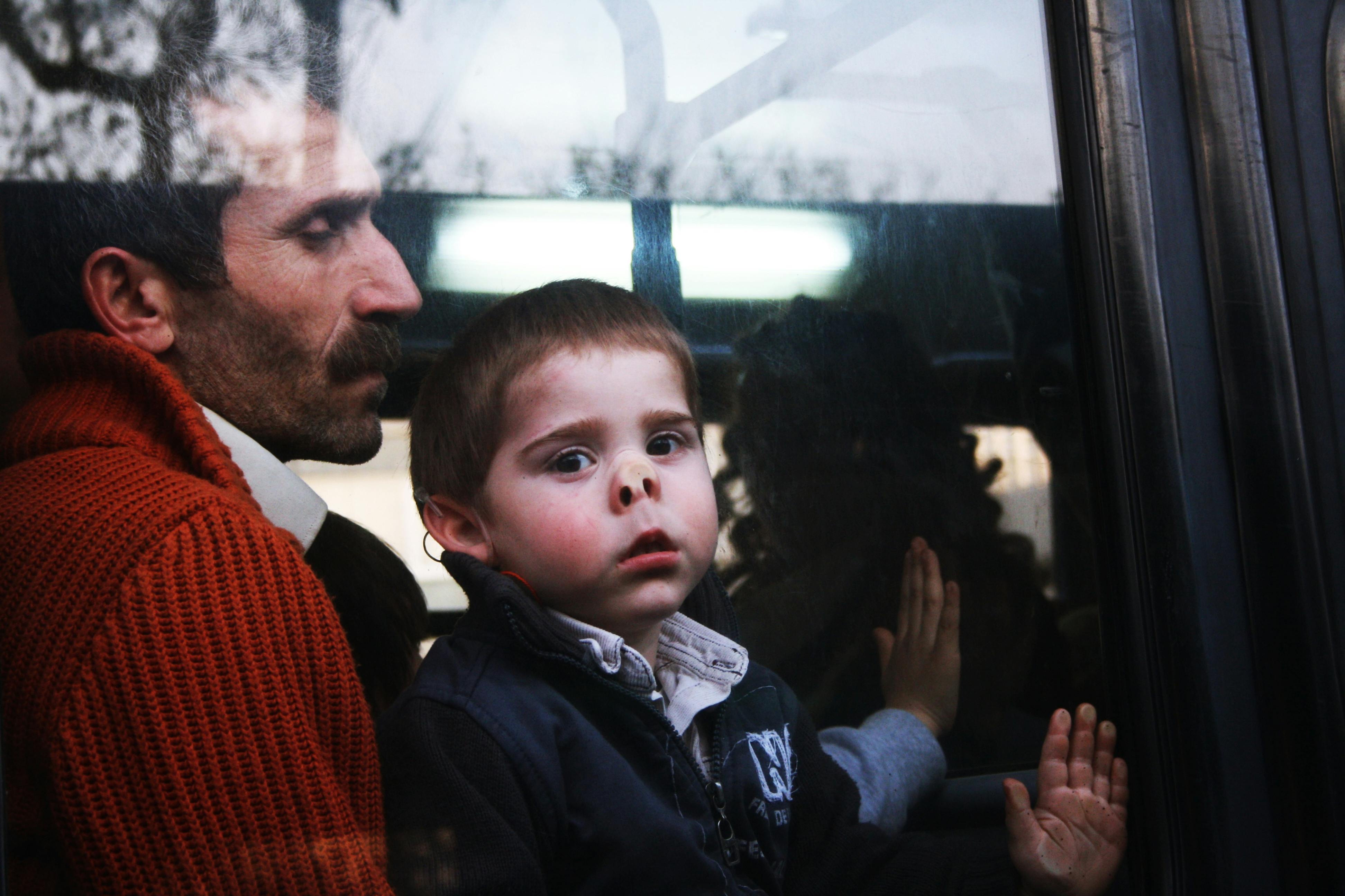 Thoughtful father and son gaze through a bus window reflecting their journey.