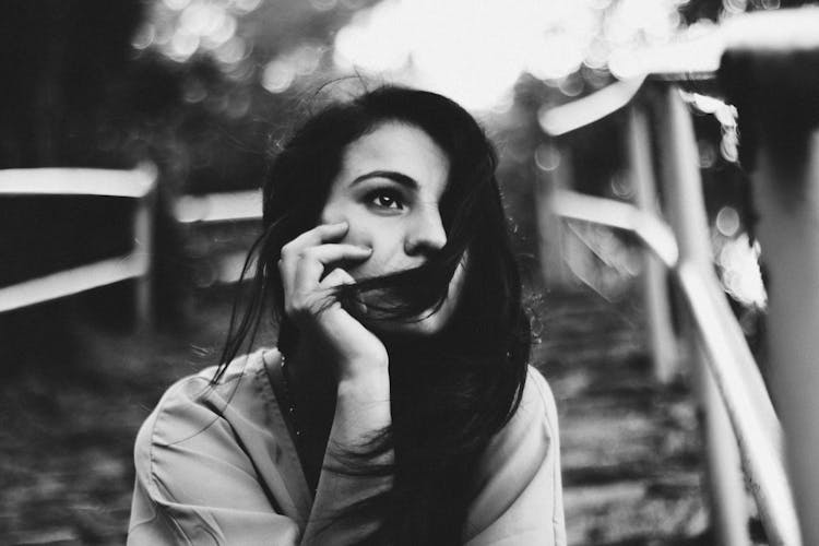 Black And White Photo Of A Young Woman Sitting Outside And Looking Away 