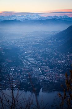 Stunning aerial view of Como, Italy, with foggy mountains and a serene lake at dusk.