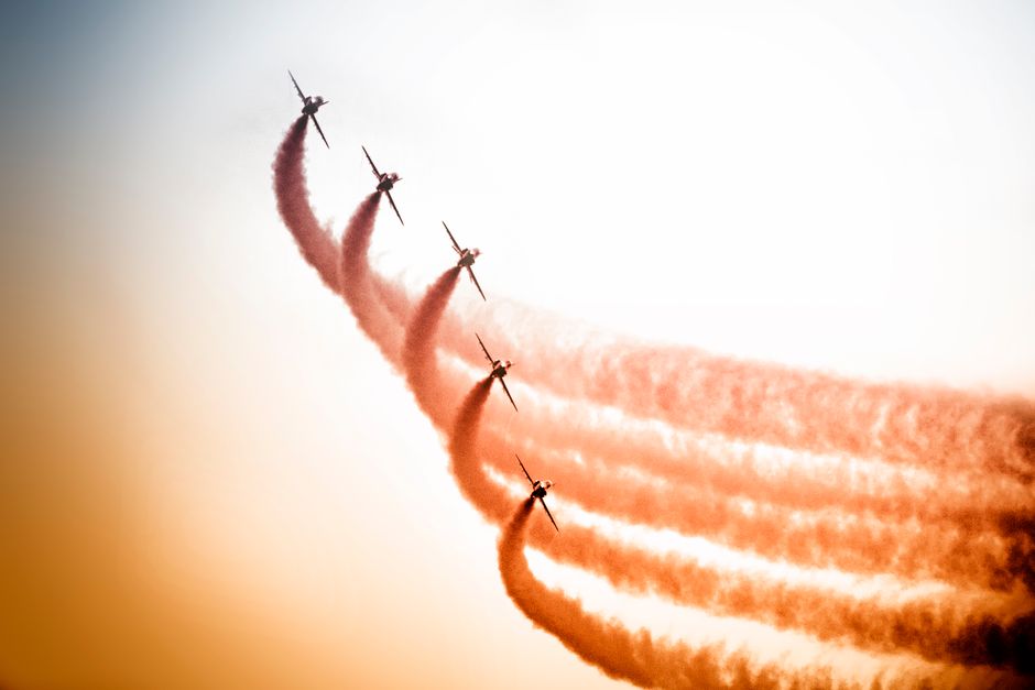 Five jets perform in a dynamic formation, leaving colorful smoke trails against a vibrant sky.