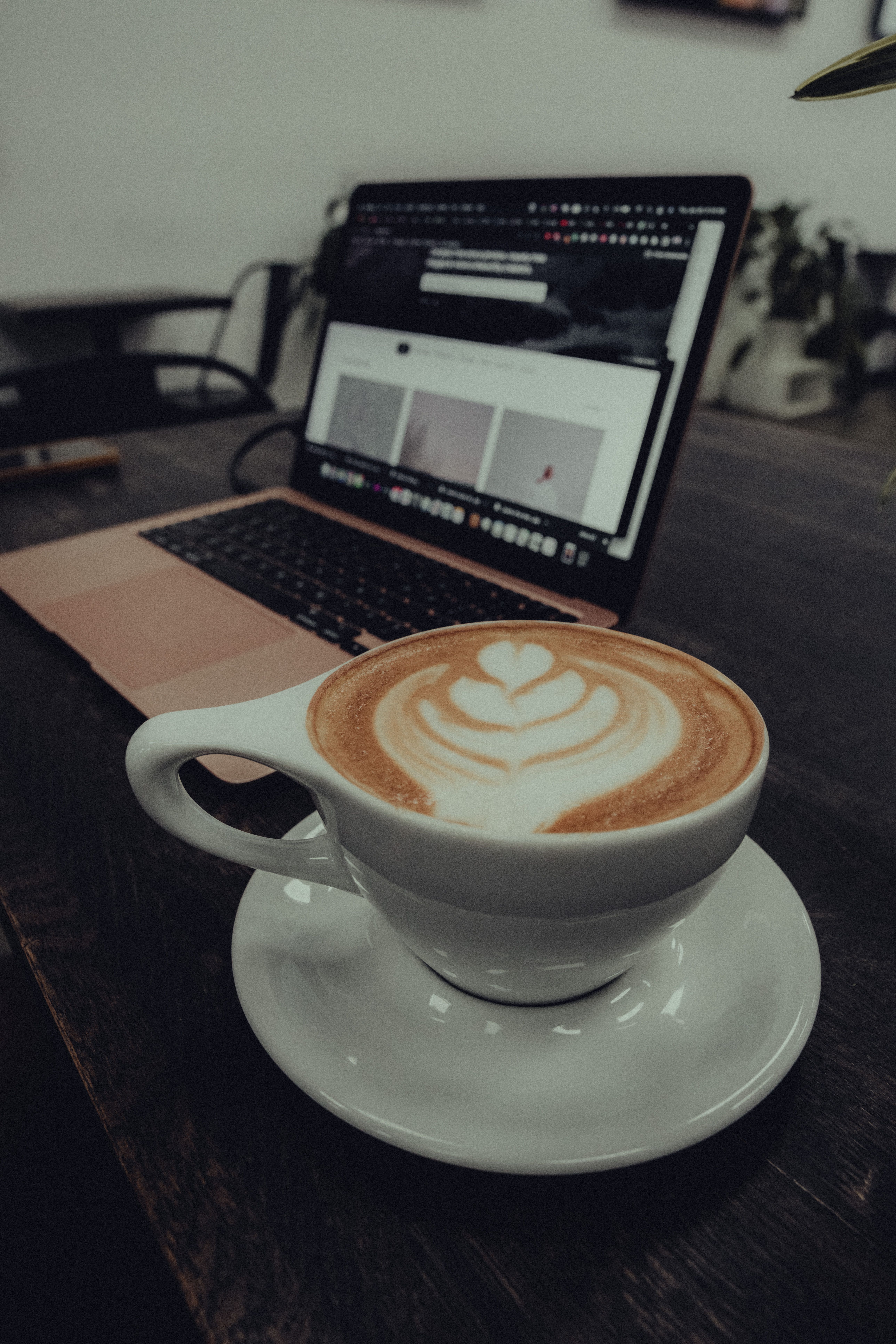 A cup of coffee with latte art next to a laptop in a café