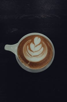 Top view of a coffee cup with intricate latte art on a dark surface.