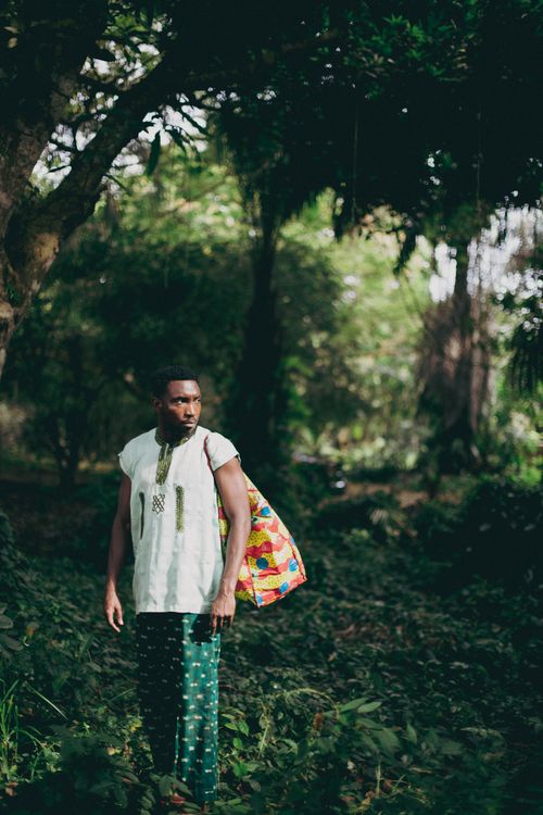 Free Portrait of a man in Lagos forest wearing traditional attire with a colorful bag, surrounded by lush greenery. Stock Photo