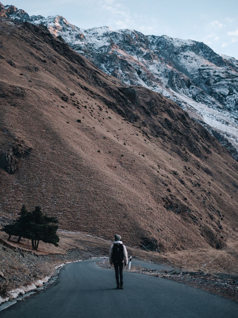 A solitary hiker walking on a winding road in the scenic Georgian mountains.