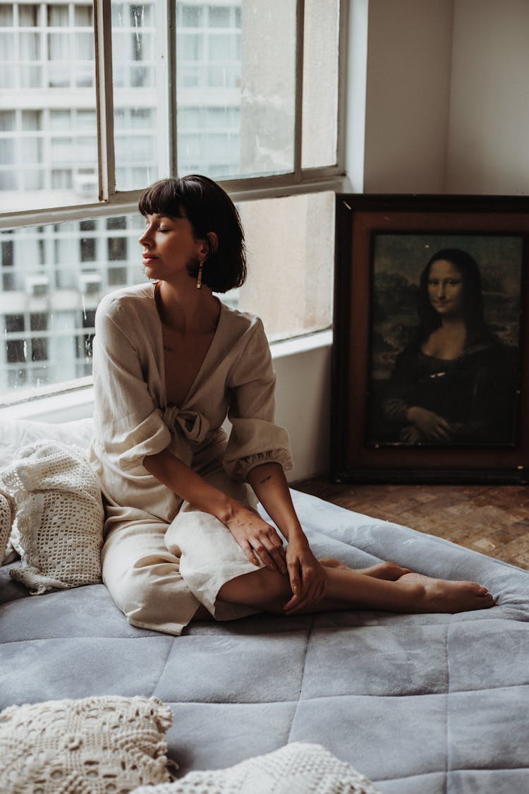 Woman Sitting On Mattress Near Window At Home