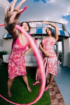 Two women in pink dresses enjoying a playful moment with a hula hoop on a sunny terrace in Orlando.