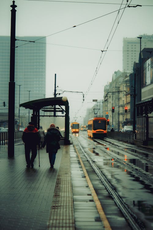 Two people walking down a wet street with a train in the background