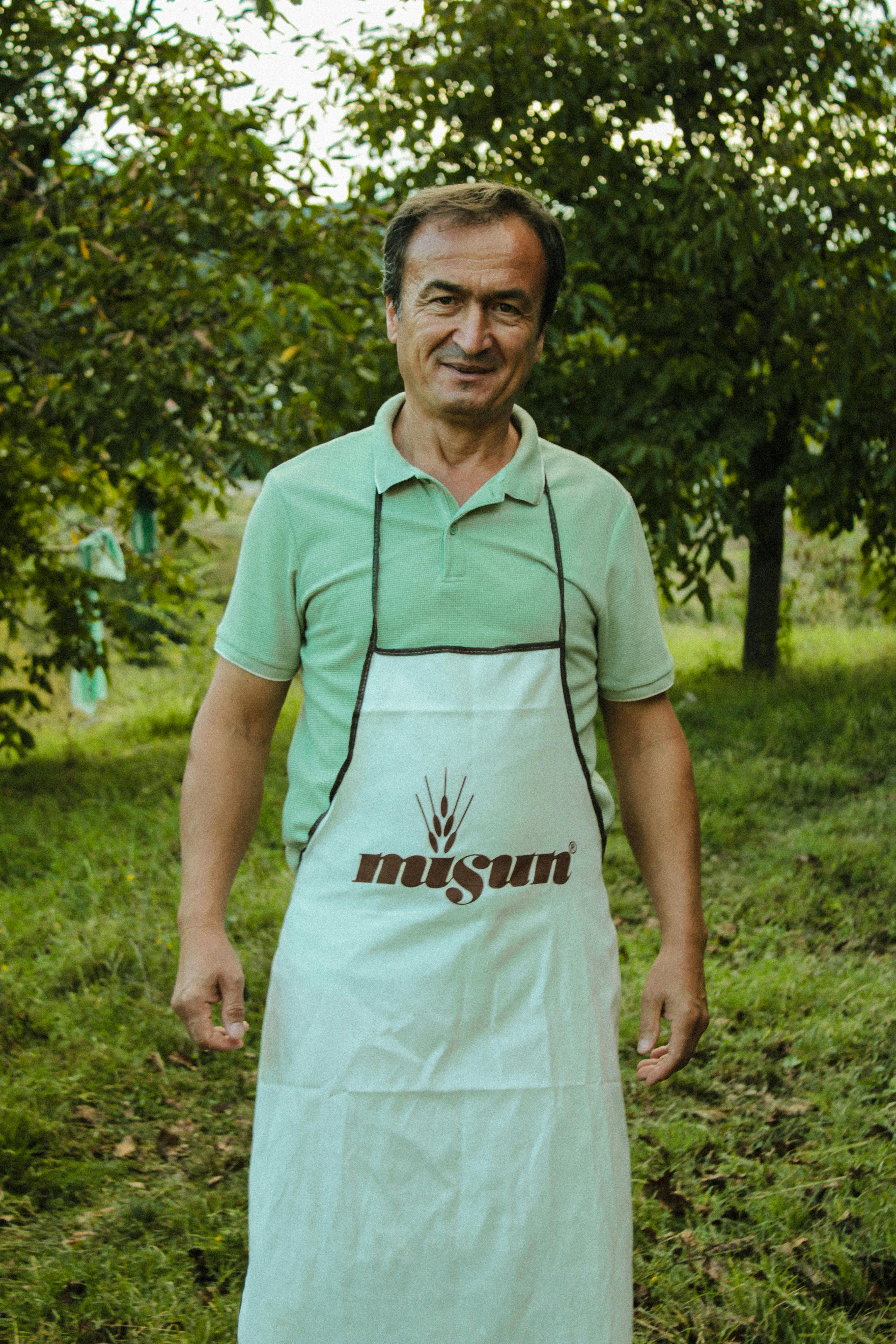 Man wearing an apron stands in a lush garden, embodying gardening lifestyle.