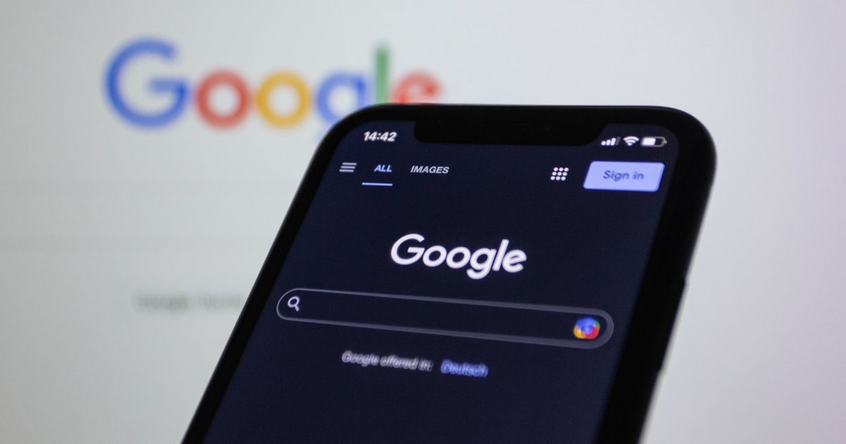 Smartphone screen showing Google search in dark mode with the Google logo in the background.