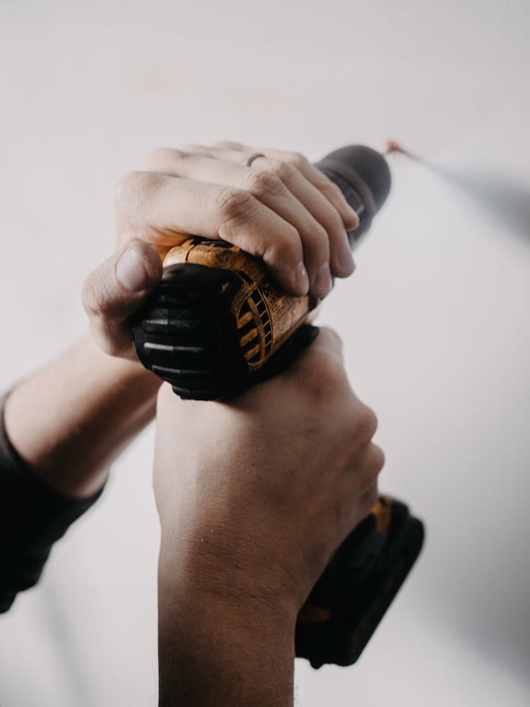 Close-up Of Man Holding Drill Against Wall