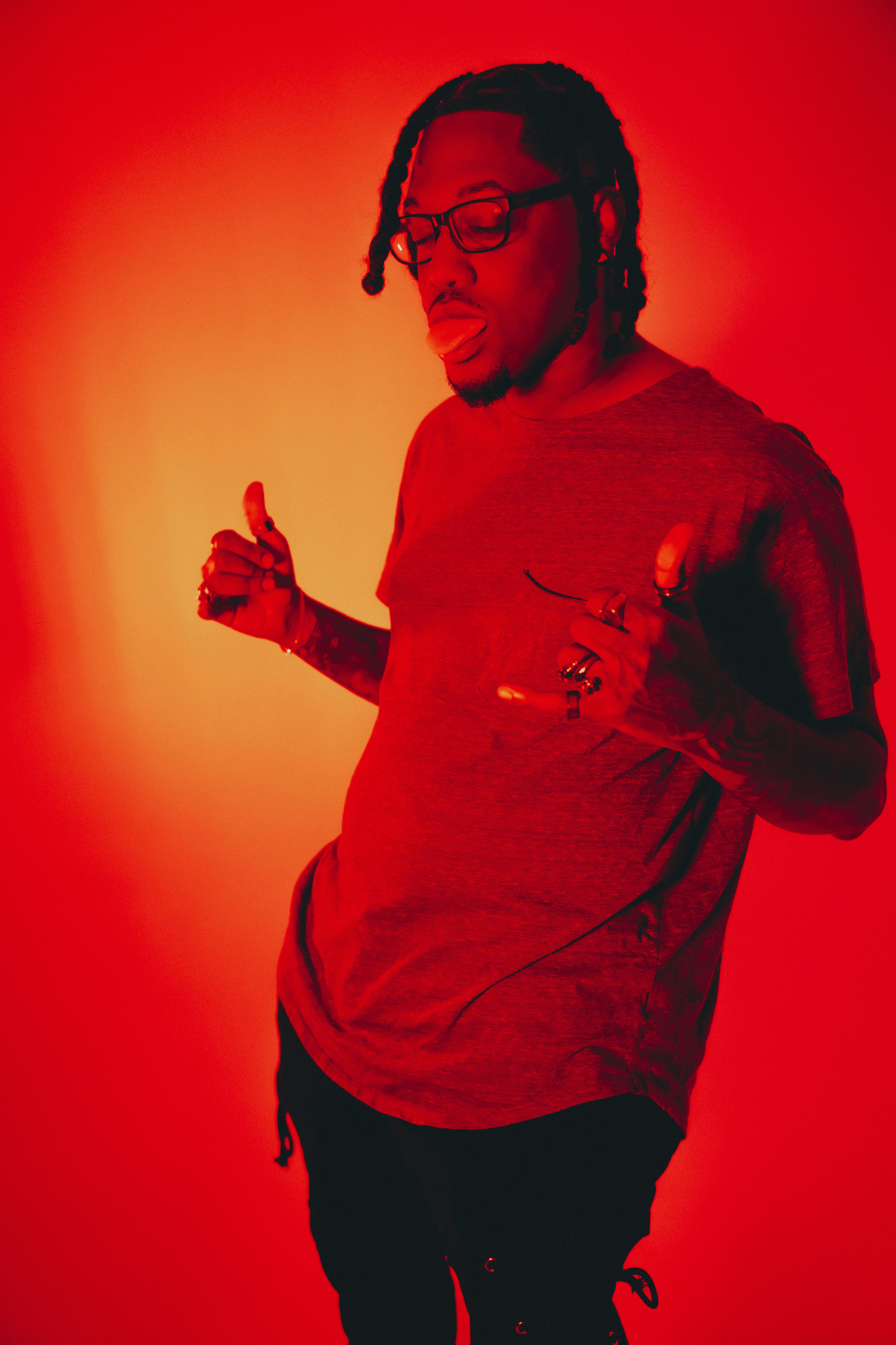 Portrait of a man posing against a vivid red background, wearing eyeglasses and a t-shirt.
