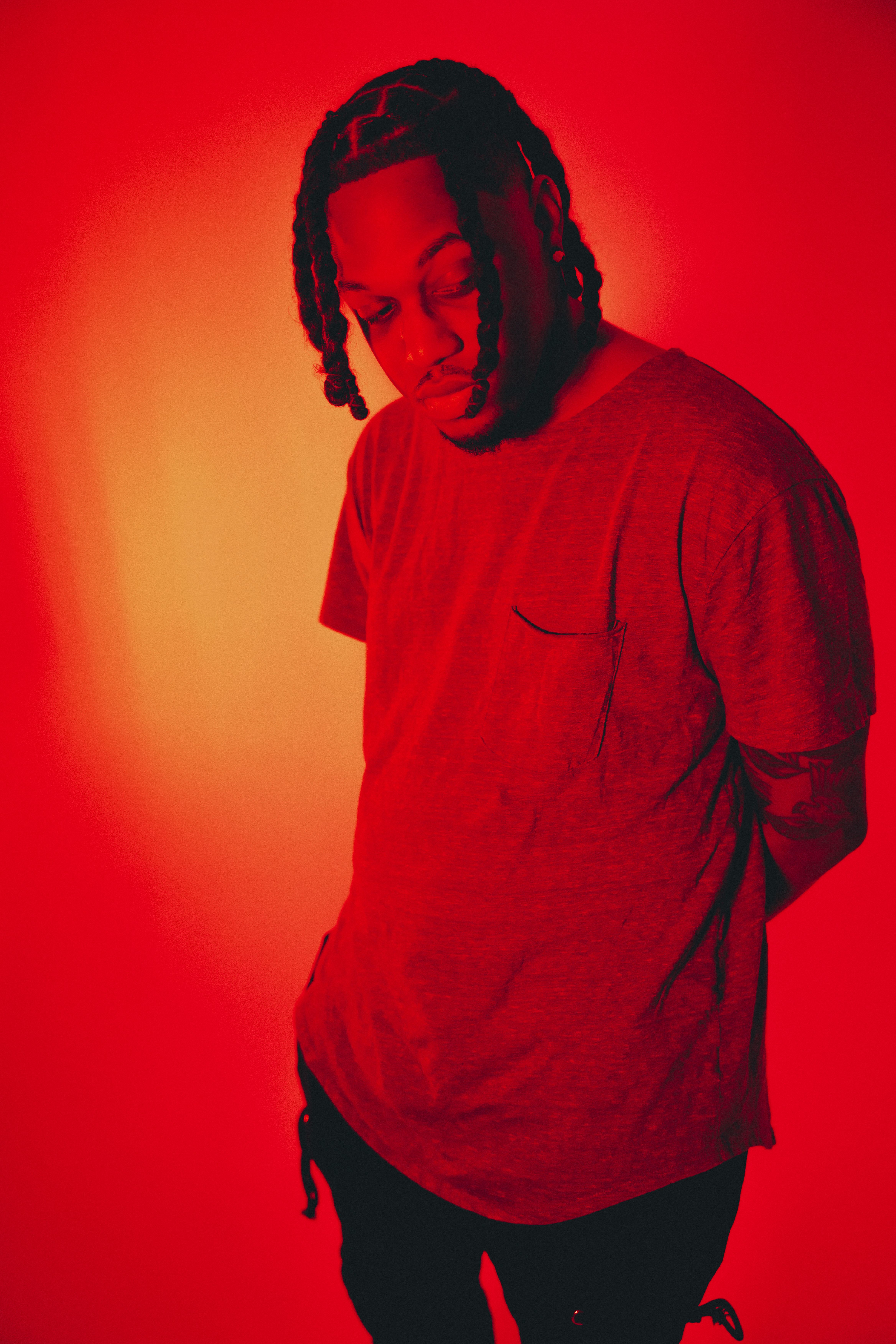 Artistic fashion portrait of a man in red lighting, showcasing casual style and unique hairstyle.