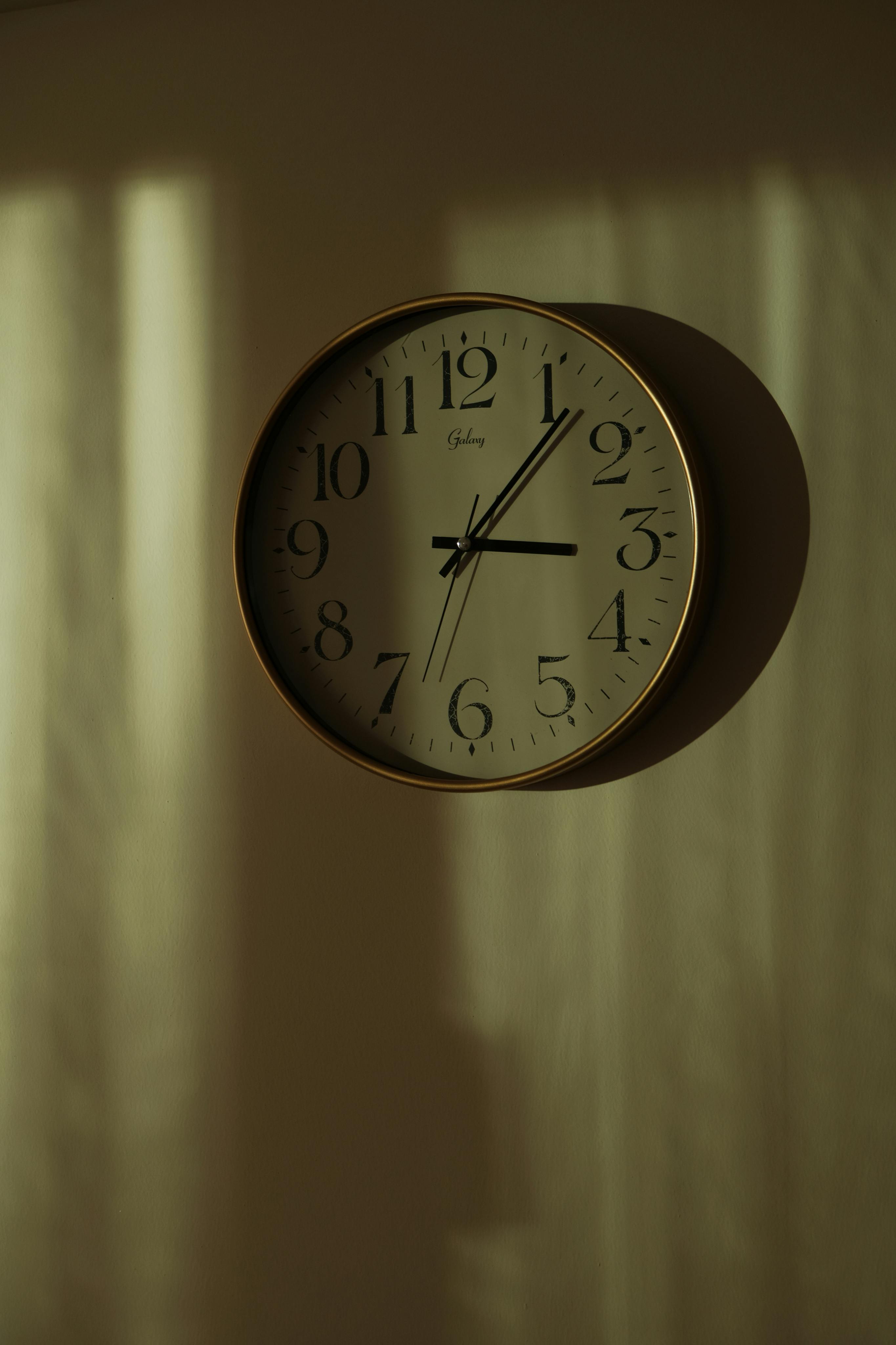 A classic round wall clock with bold numerals, casting artistic shadows on a softly lit wall.