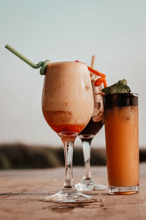 Free Three vibrant cocktails with straws and garnish on a wooden table outdoors in Angola. Stock Photo