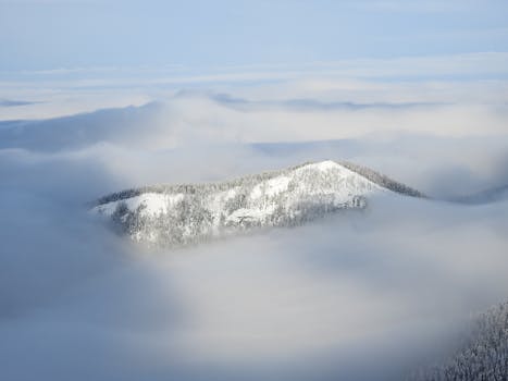 A serene view of a snowy mountain peak surrounded by clouds in winter.