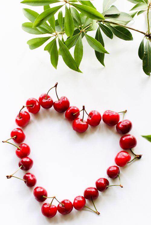 Free A creative heart-shaped arrangement of cherries with leafy branches, perfect for romantic and food themes. Stock Photo