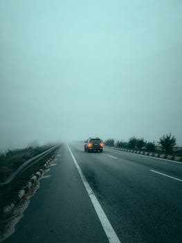 A lone car drives on a foggy highway creating an atmospheric travel scene.