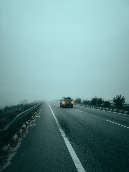 Free A lone car drives on a foggy highway creating an atmospheric travel scene. Stock Photo