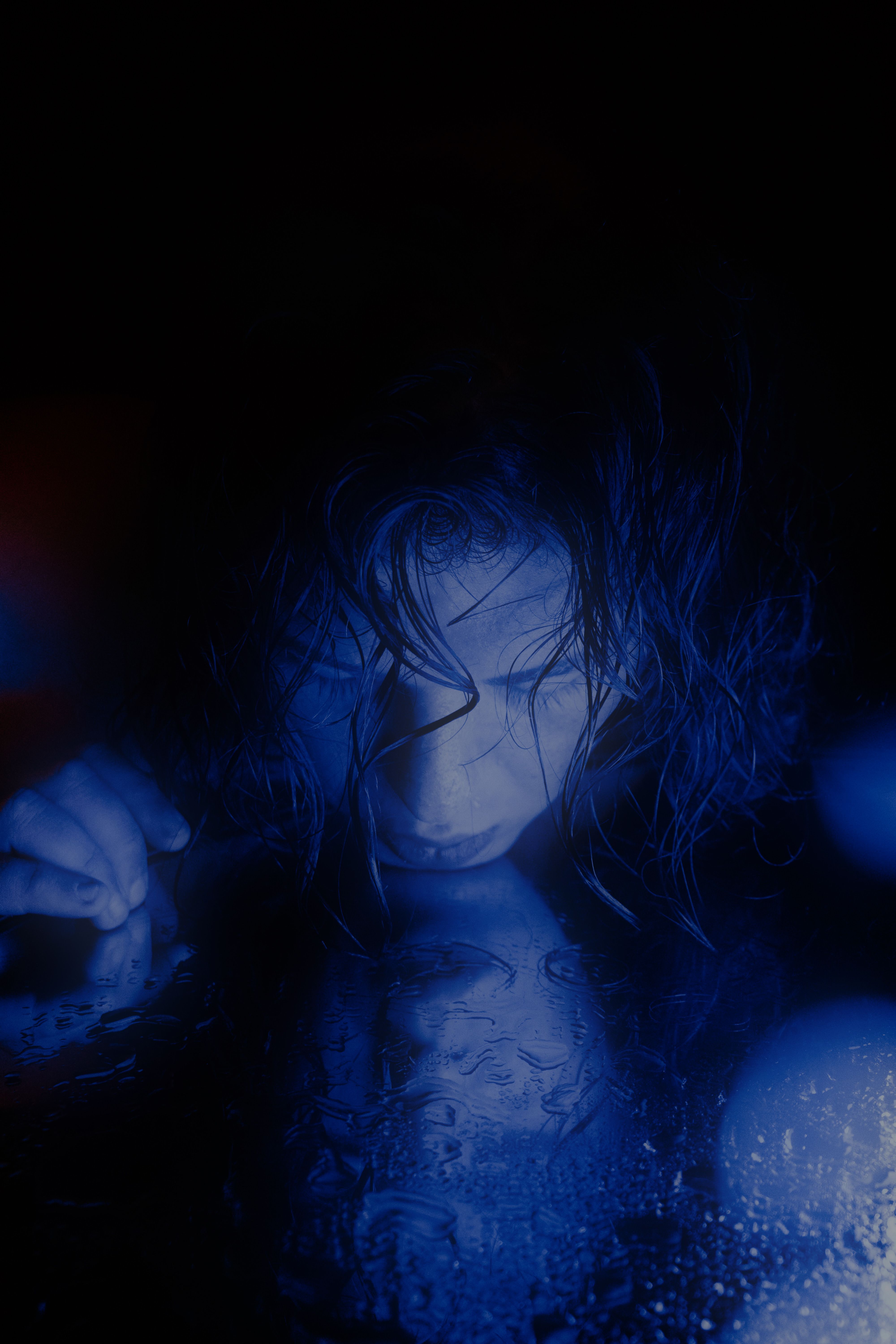 A dramatic portrait of a woman gazing at her reflection, immersed in blue light.