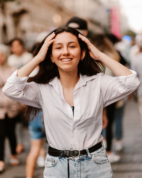 Free Young woman smiling with hands in hair, standing on a bustling street in Istanbul. Stock Photo
