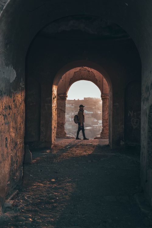Free A person with a backpack walking under an archway at sunset, casting a silhouette. Stock Photo