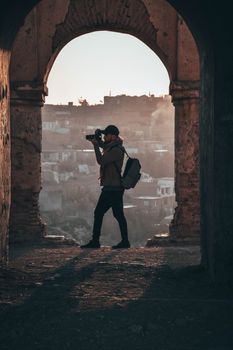 Silhouette of a man with a camera in a rustic archway overlooking a misty town.