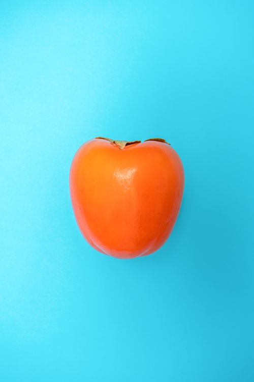 Free Close-up of a ripe persimmon against a vibrant blue background for healthy eating concepts. Stock Photo