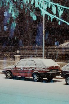 A classic red car parked on a snowy street during a winter snowstorm at night.