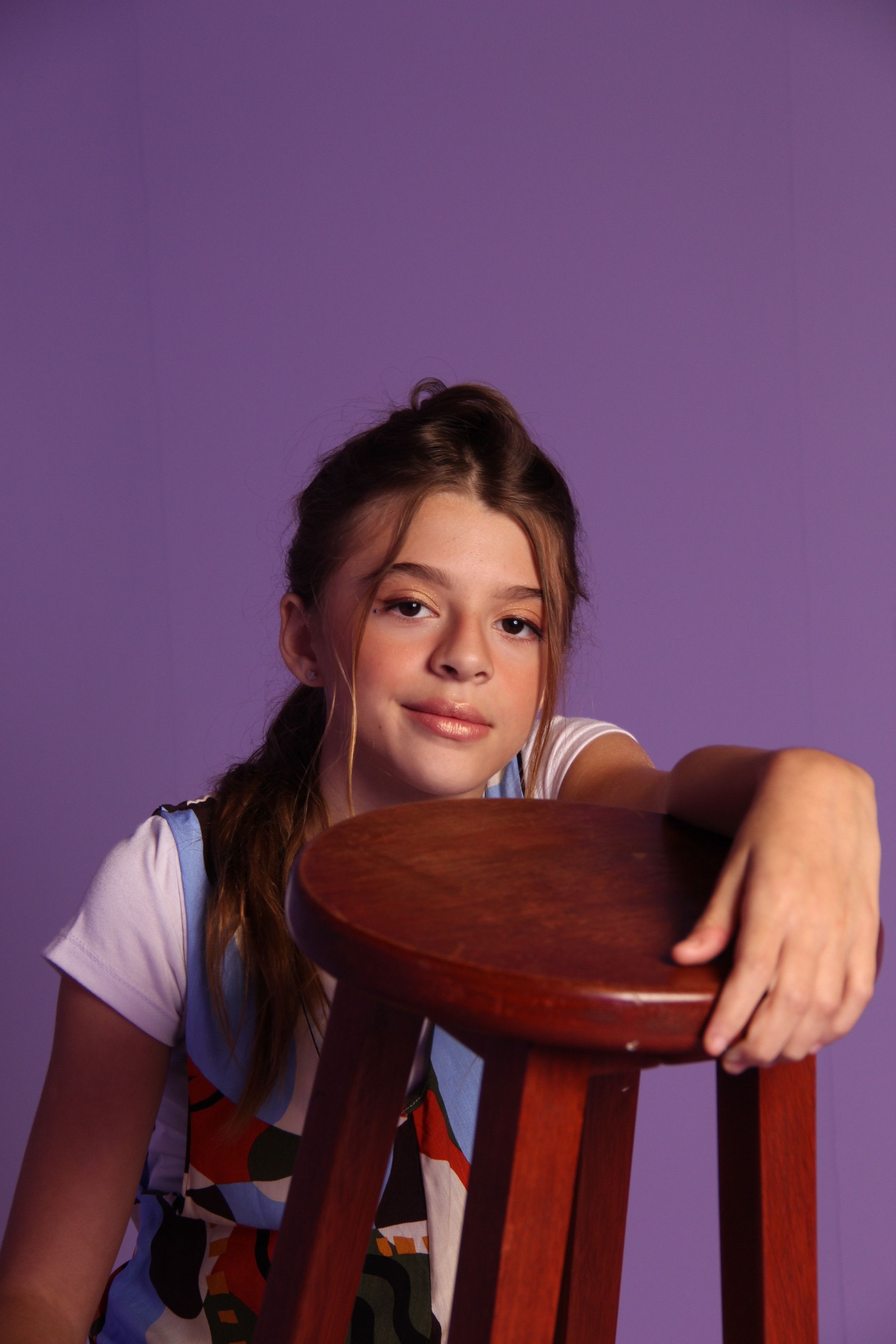 Young girl posing with a wooden stool in a studio setting. Vibrant and stylish.