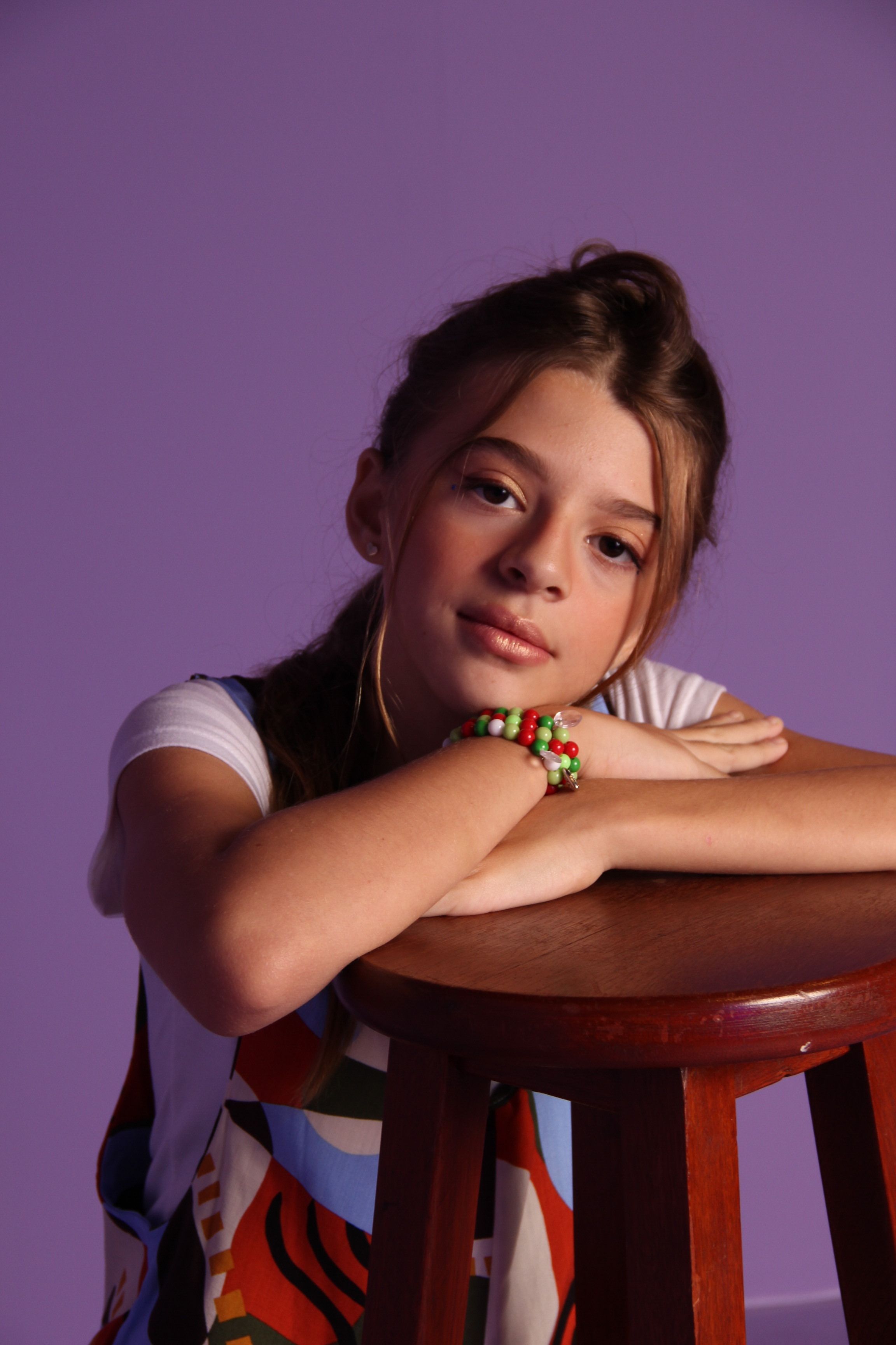 Captivating studio portrait of a young girl with brunette hair posing against a purple backdrop.
