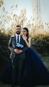 A couple poses elegantly outdoors in a navy-themed wedding attire, embracing love.